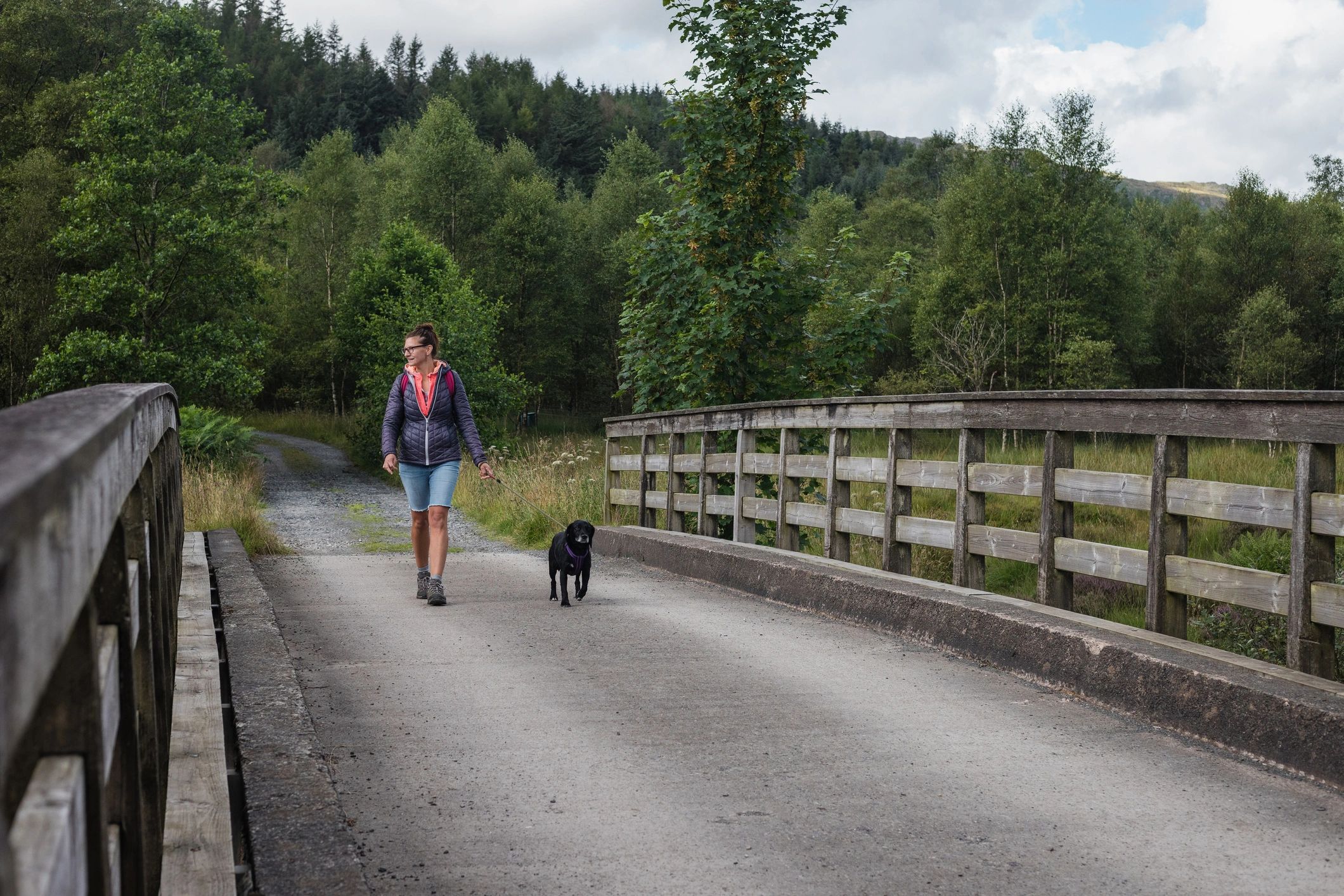 Woman walking a dog across a bridge on a trail