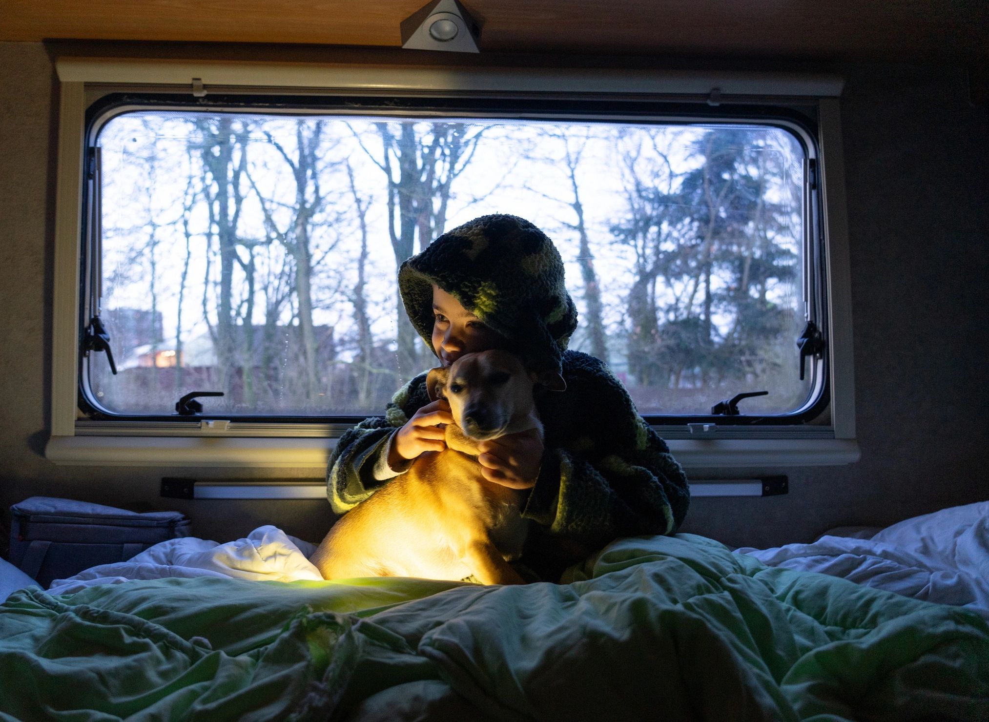 Child and dog relaxing in a motorhome bed at night